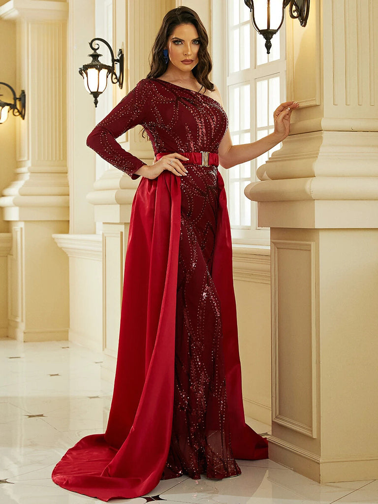 An Elegant burgundy one-shoulder gown featuring intricate sequin detailing, a gold belt accent, and a dramatic cape for a regal and sophisticated look.