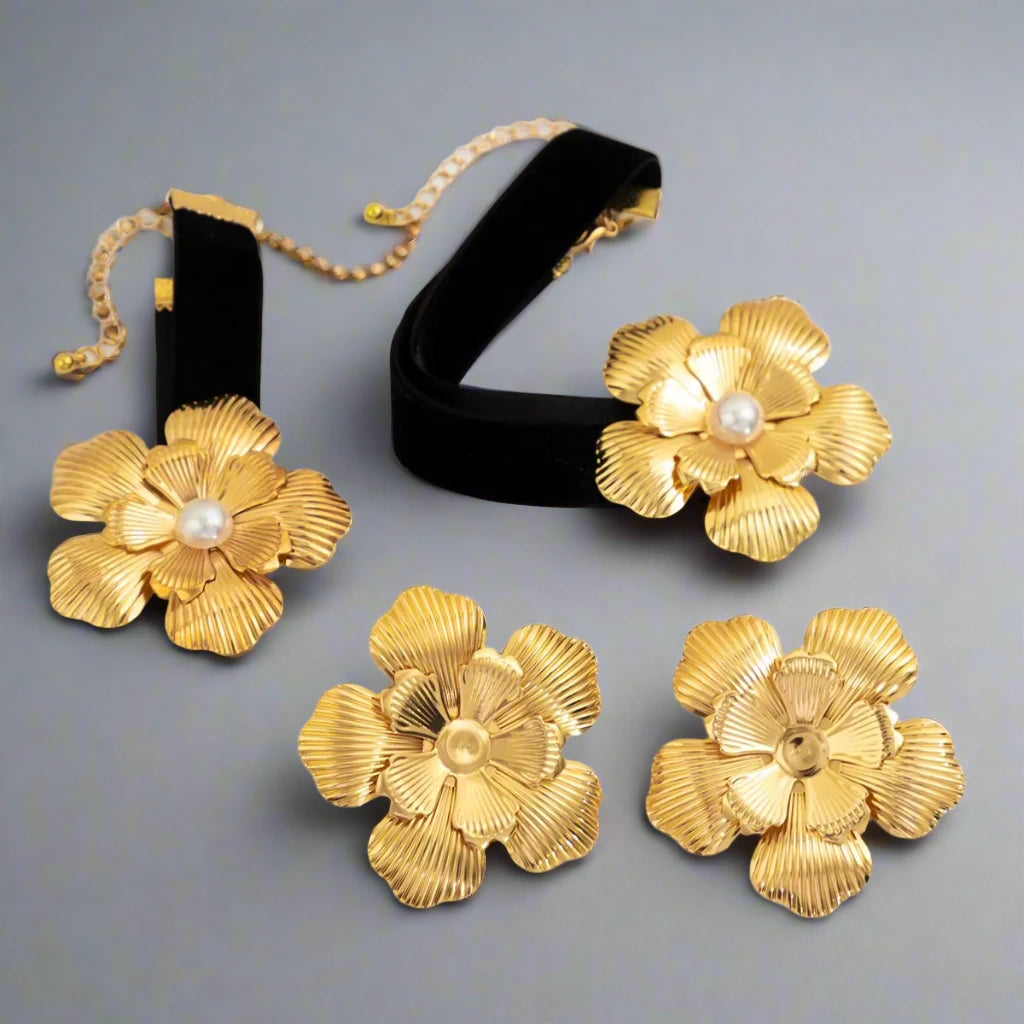 Striking jewelry set featuring bold gold-tone floral designs, including statement earrings, a choker, and a bracelet, each adorned with a detailed flower motif and a pearl center, creating a glamorous and cohesive look.