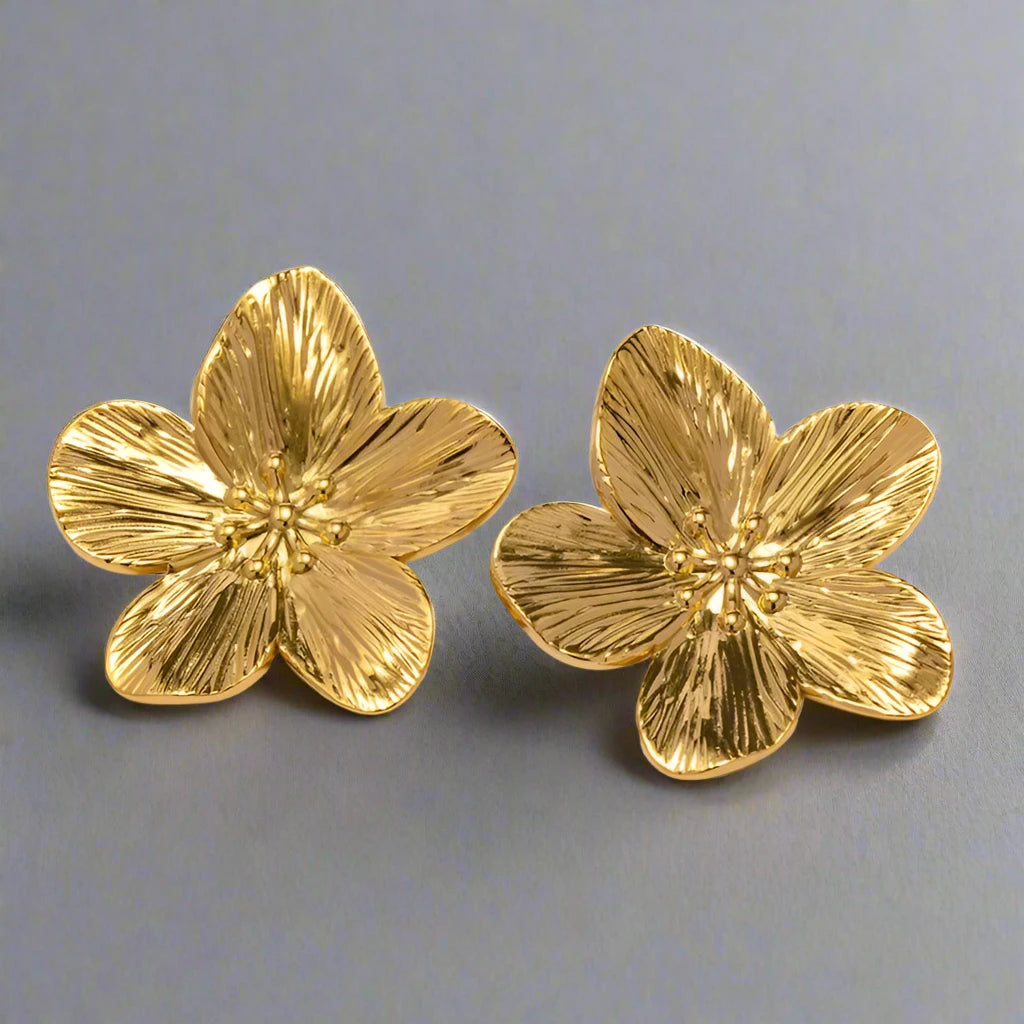 gold-tone flower earrings with intricate petal detailing. The earrings feature a textured surface, mimicking the natural veins of flower petals, and have small, delicate bead-like accents in the center, adding an elegant and feminine touch.







