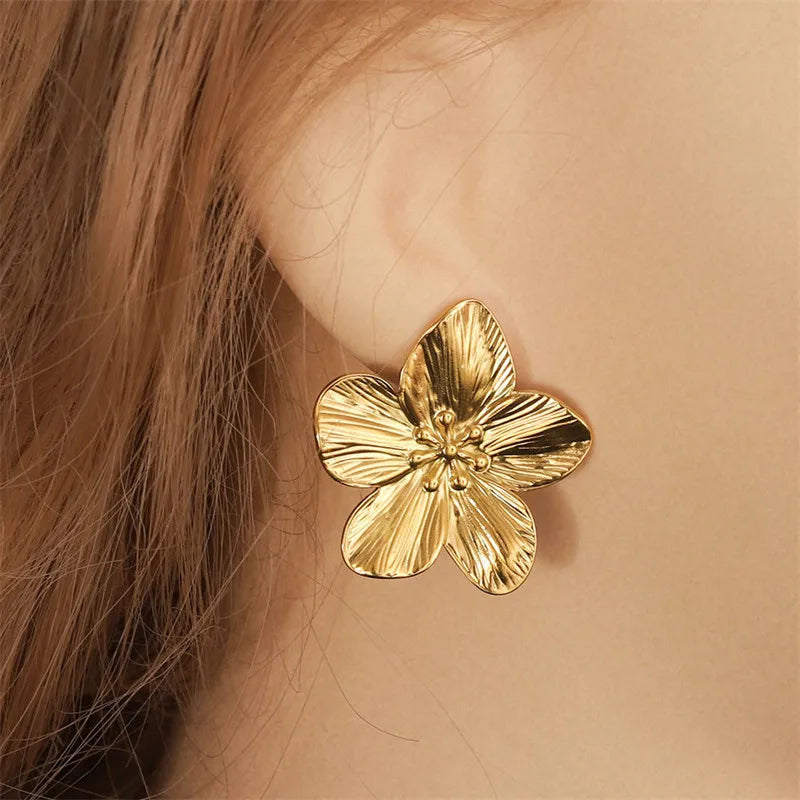 gold-tone flower earrings with intricate petal detailing. The earrings feature a textured surface, mimicking the natural veins of flower petals, and have small, delicate bead-like accents in the center, adding an elegant and feminine touch.







