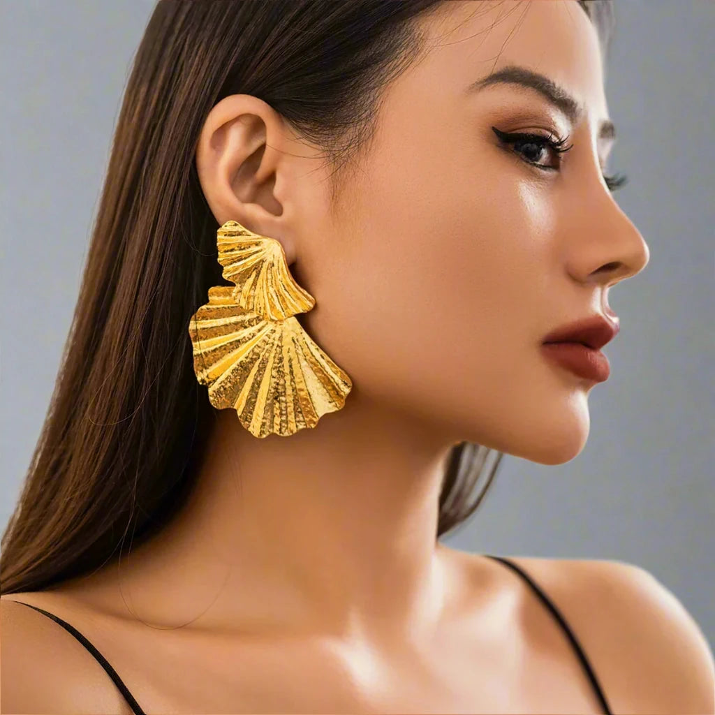 Gold-tone statement earring with a textured, fan-like design. The earring features multiple layered, shell-inspired shapes with intricate ridged details, adding an elegant yet bold look. The matte finish and unique structure give the earring a refined, sculptural aesthetic.