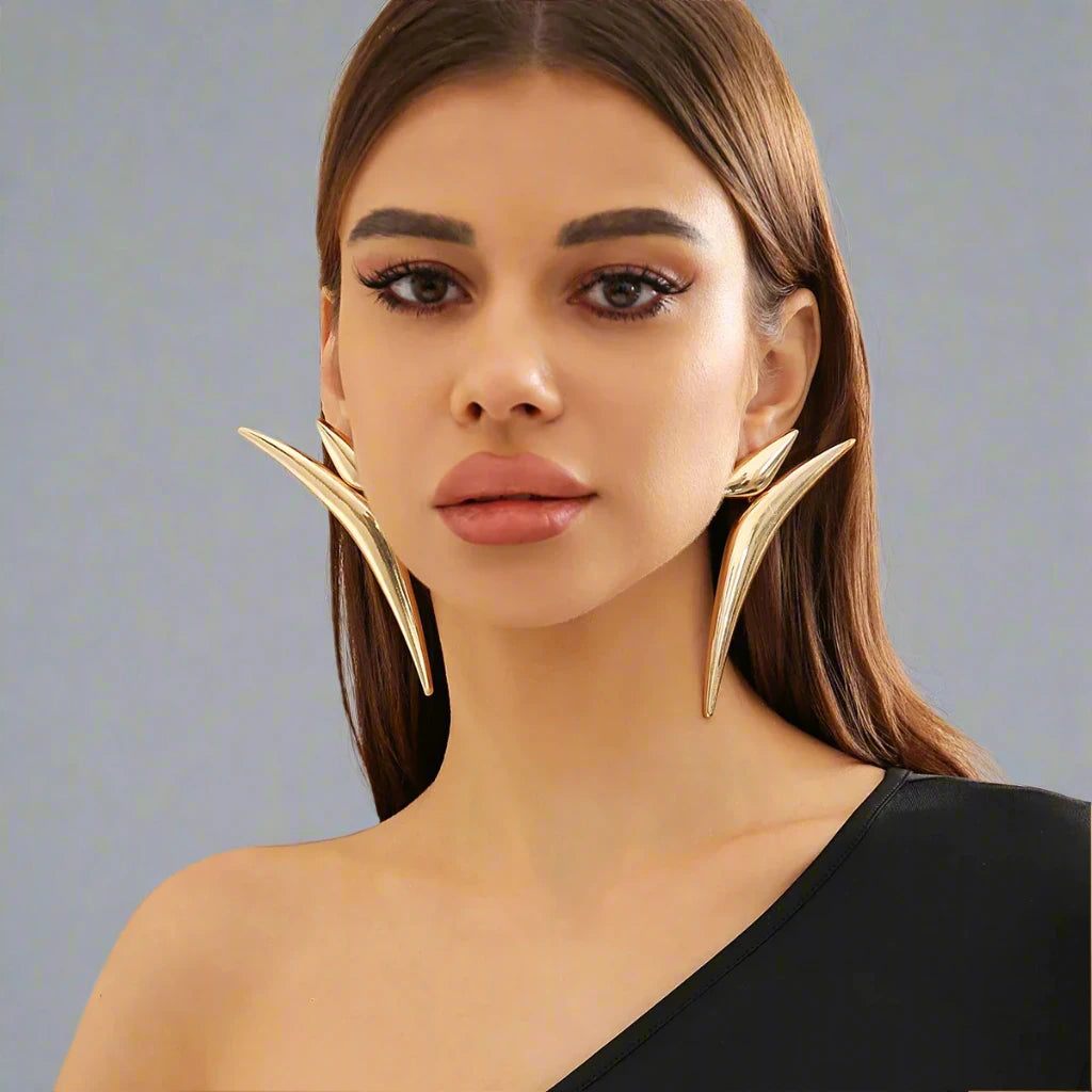 Striking gold-tone earrings featuring a bold, angular design that extends dramatically along the ear, creating a modern and edgy statement piece.