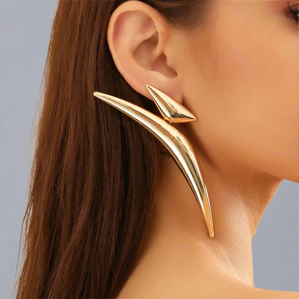 Striking gold-tone earrings featuring a bold, angular design that extends dramatically along the ear, creating a modern and edgy statement piece.