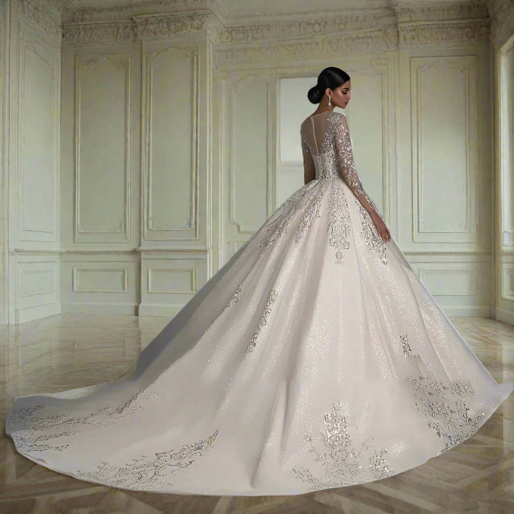 Elegant bridal gown featuring a ball gown silhouette. The dress is adorned with intricate silver embroidery and beading, creating a luxurious and sparkling effect. It has a sweetheart neckline overlaid with sheer fabric forming long, fitted lace sleeves and an illusion neckline. The full skirt flows into a dramatic train, enhancing the gown's regal appearance. The light ivory color adds a soft and romantic touch, making it a perfect choice for a formal wedding.