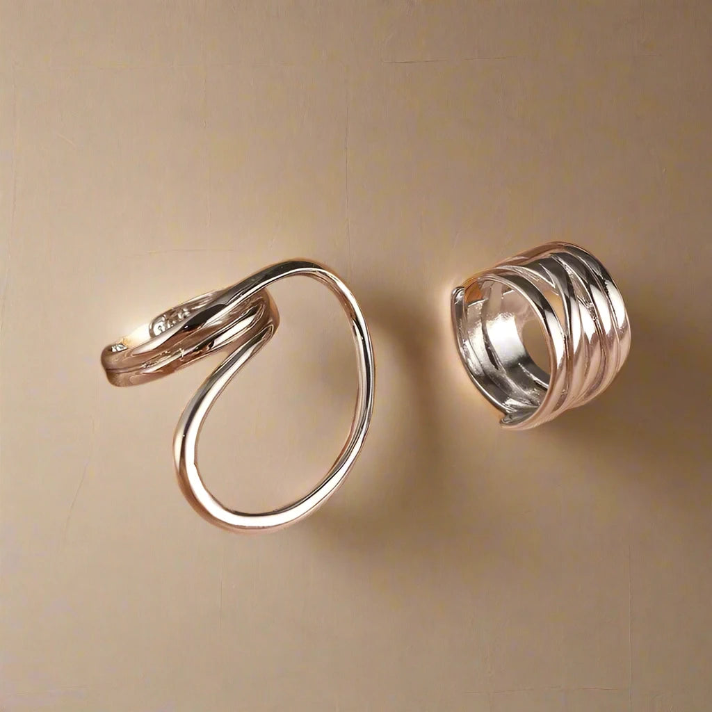 A set of two modern silver-tone rings featuring unique, abstract designs—one with a bold, open loop and the other with a layered, wrap-around style—creating a chic and artistic statement on the hand.