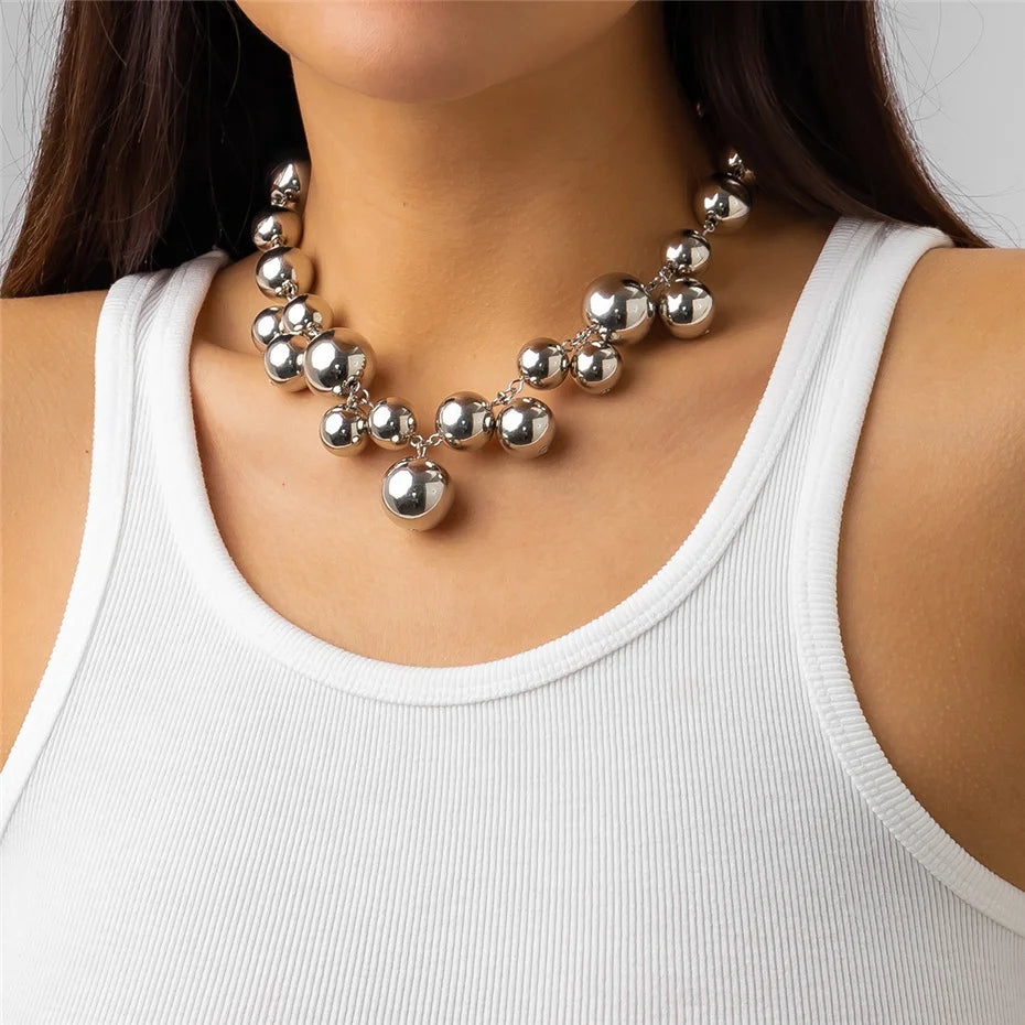 Bold Silver-tone statement necklace with large, glossy metallic beads of varying sizes. The necklace adds a glamorous and chic touch to her simple white tank top.







