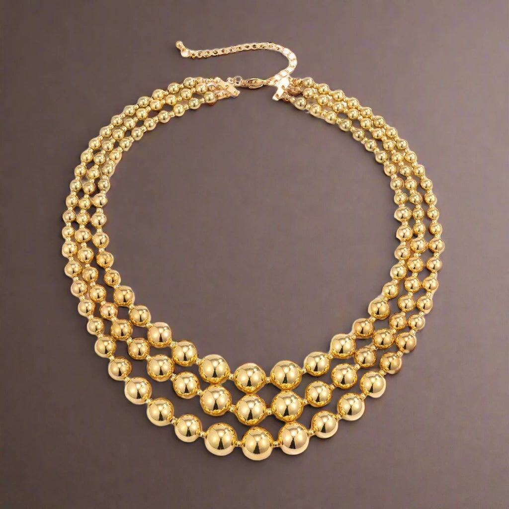 A stunning multi-layered necklace featuring large, polished gold-tone beads, creating a bold and glamorous statement piece that adds elegance and sophistication to any outfit.