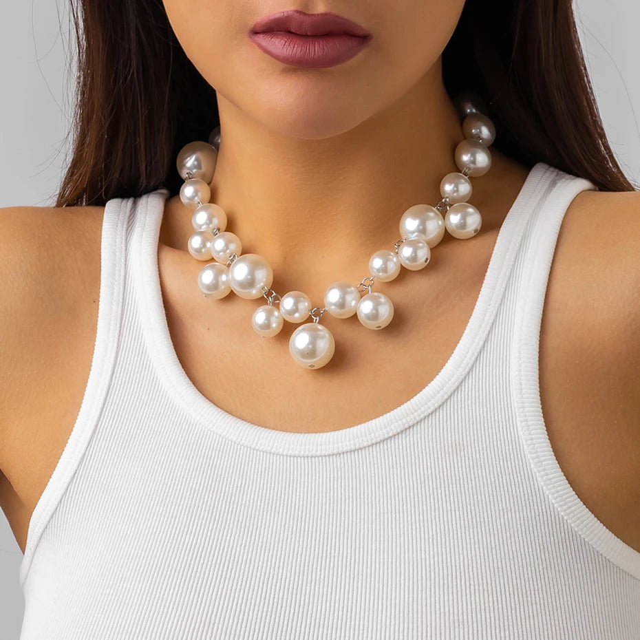 Bold White-tone statement necklace with large, glossy metallic beads of varying sizes. The necklace adds a glamorous and chic touch to her simple white tank top.







