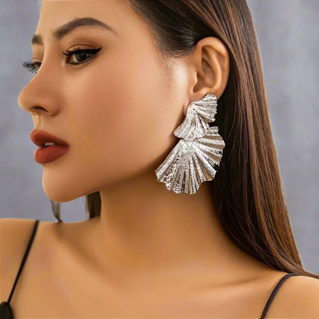 Silver-tone statement earring with a textured, fan-like design. The earring features multiple layered, shell-inspired shapes with intricate ridged details, adding an elegant yet bold look. The matte finish and unique structure give the earring a refined, sculptural aesthetic.