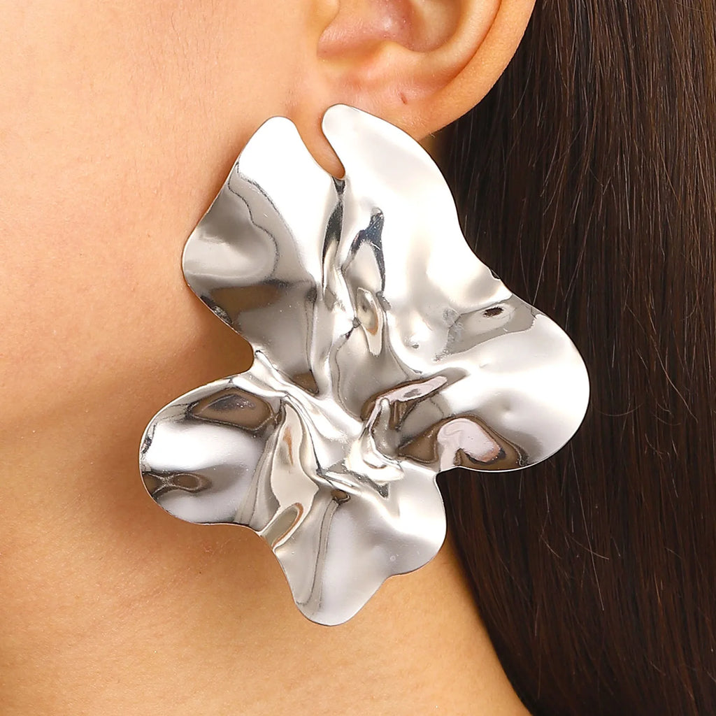 Large, silver-tone Floral sculptural earring. The earring has a fluid, abstract flower-like design with a shiny, reflective surface, adding a bold, artistic touch to her look.