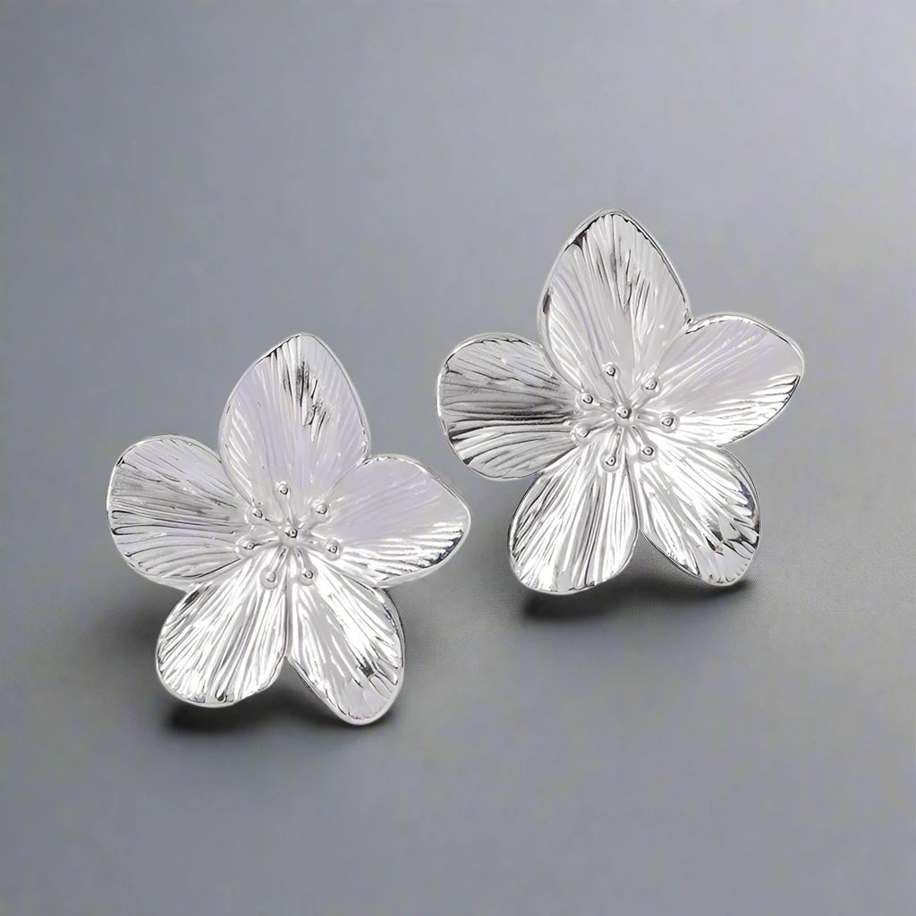 Silver-tone flower earrings with intricate petal detailing. The earrings feature a textured surface, mimicking the natural veins of flower petals, and have small, delicate bead-like accents in the center, adding an elegant and feminine touch.







