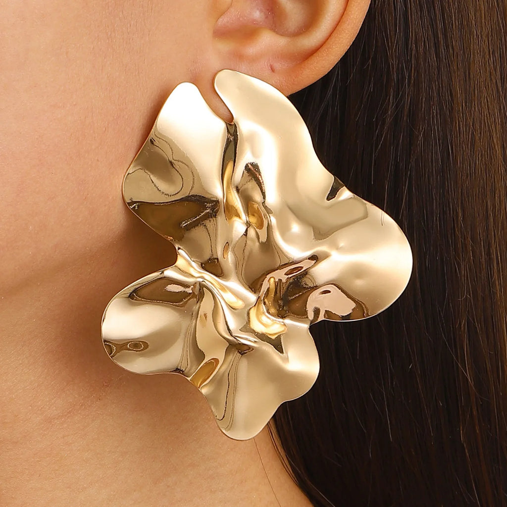 Large, Gold-tone Floral sculptural earring. The earring has a fluid, abstract flower-like design with a shiny, reflective surface, adding a bold, artistic touch to her look.