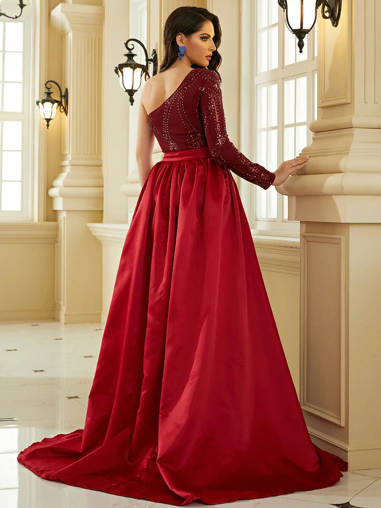 An Elegant burgundy one-shoulder gown featuring intricate sequin detailing, a gold belt accent, and a dramatic cape for a regal and sophisticated look.