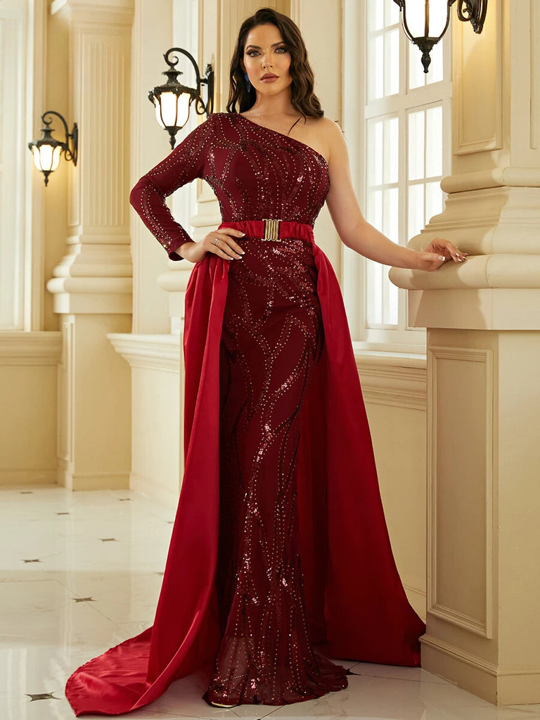 An Elegant burgundy one-shoulder gown featuring intricate sequin detailing, a gold belt accent, and a dramatic cape for a regal and sophisticated look.