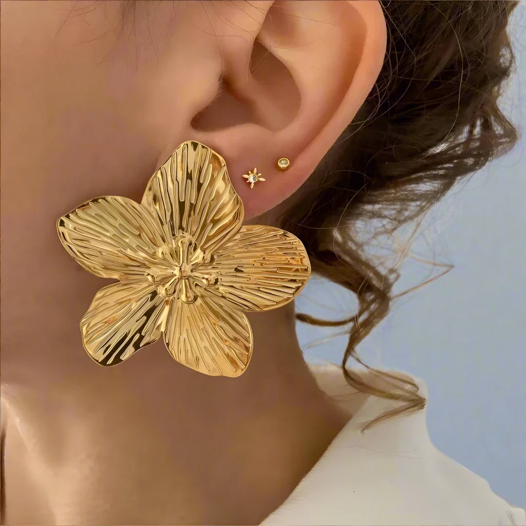 gold-tone flower earrings with intricate petal detailing. The earrings feature a textured surface, mimicking the natural veins of flower petals, and have small, delicate bead-like accents in the center, adding an elegant and feminine touch.







